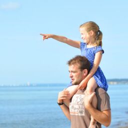 Vater und Tochter im Sommerurlaub in Grömitz, Kind zeigt auf das Meer